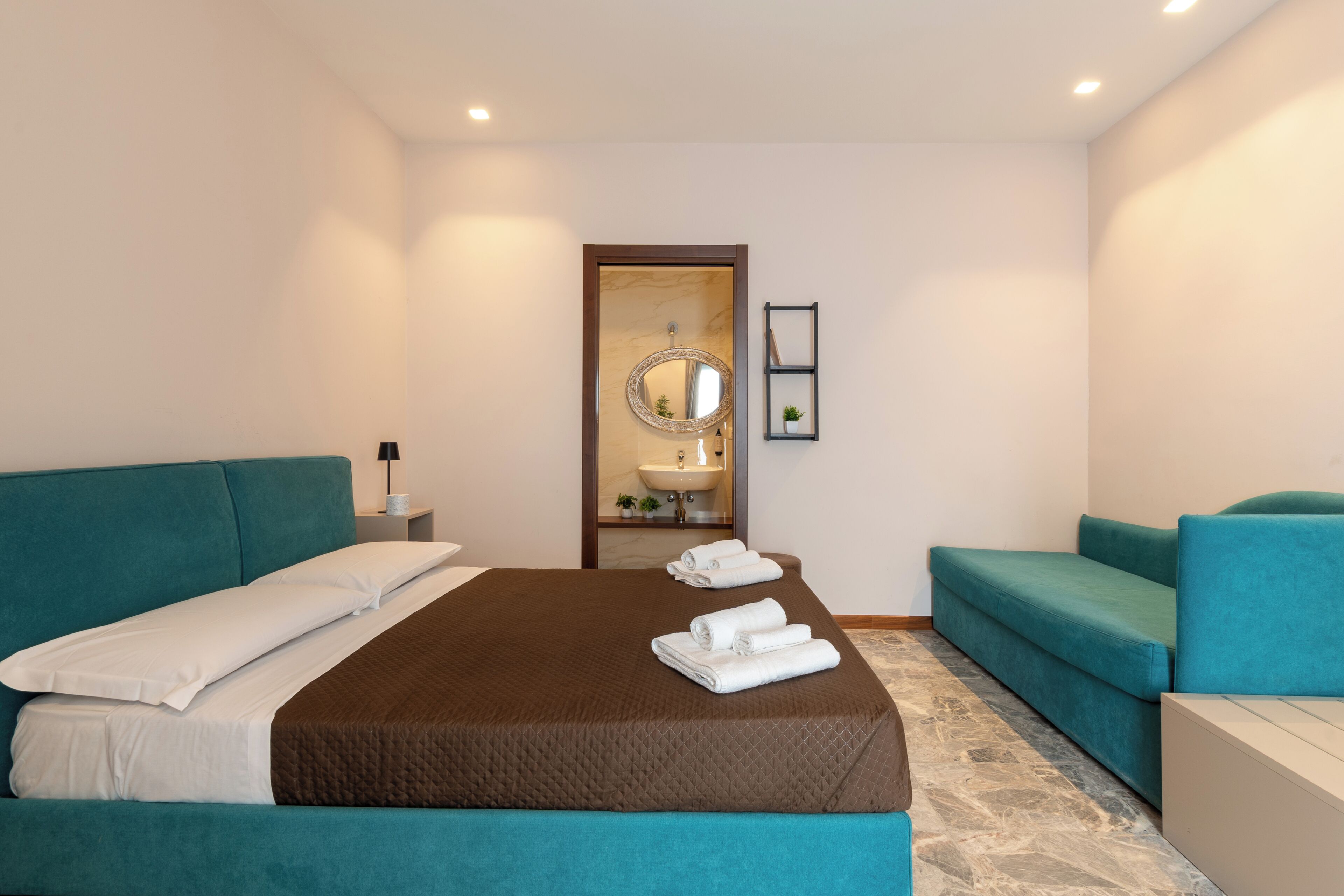 A hotel room with a large bed, two sofas, a bathroom with a mirror, and a sink.