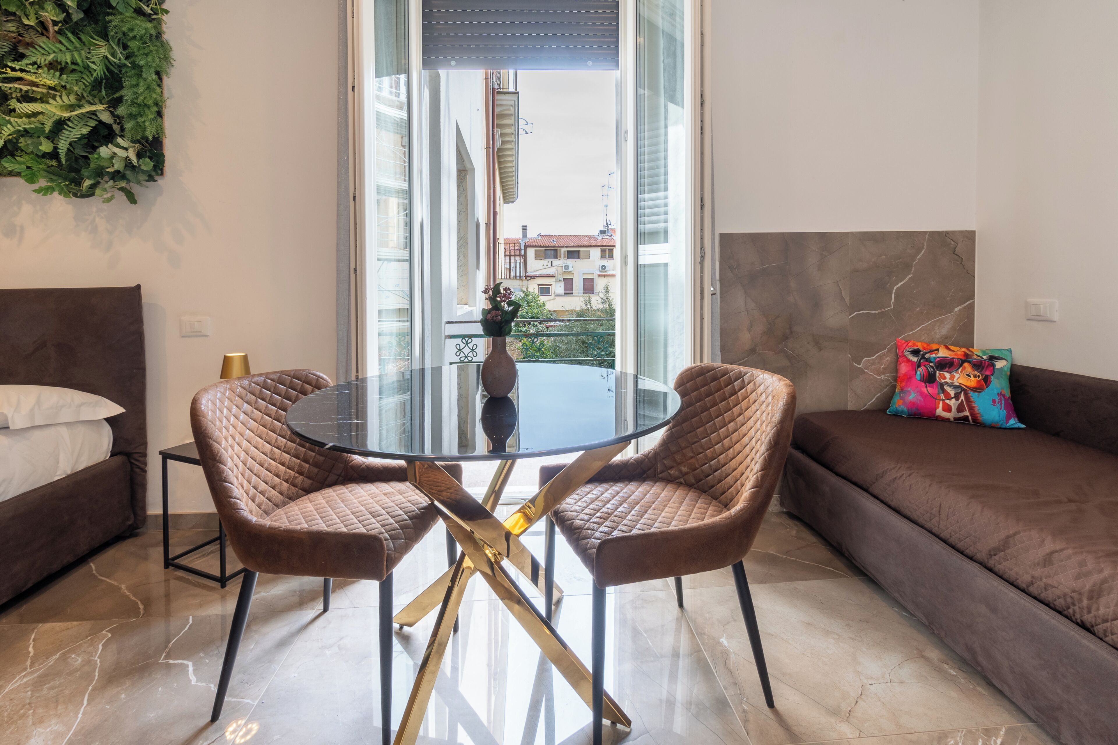 A modern living room with a glass table, two brown cushioned chairs, a brown sofa, and a decorative plant.