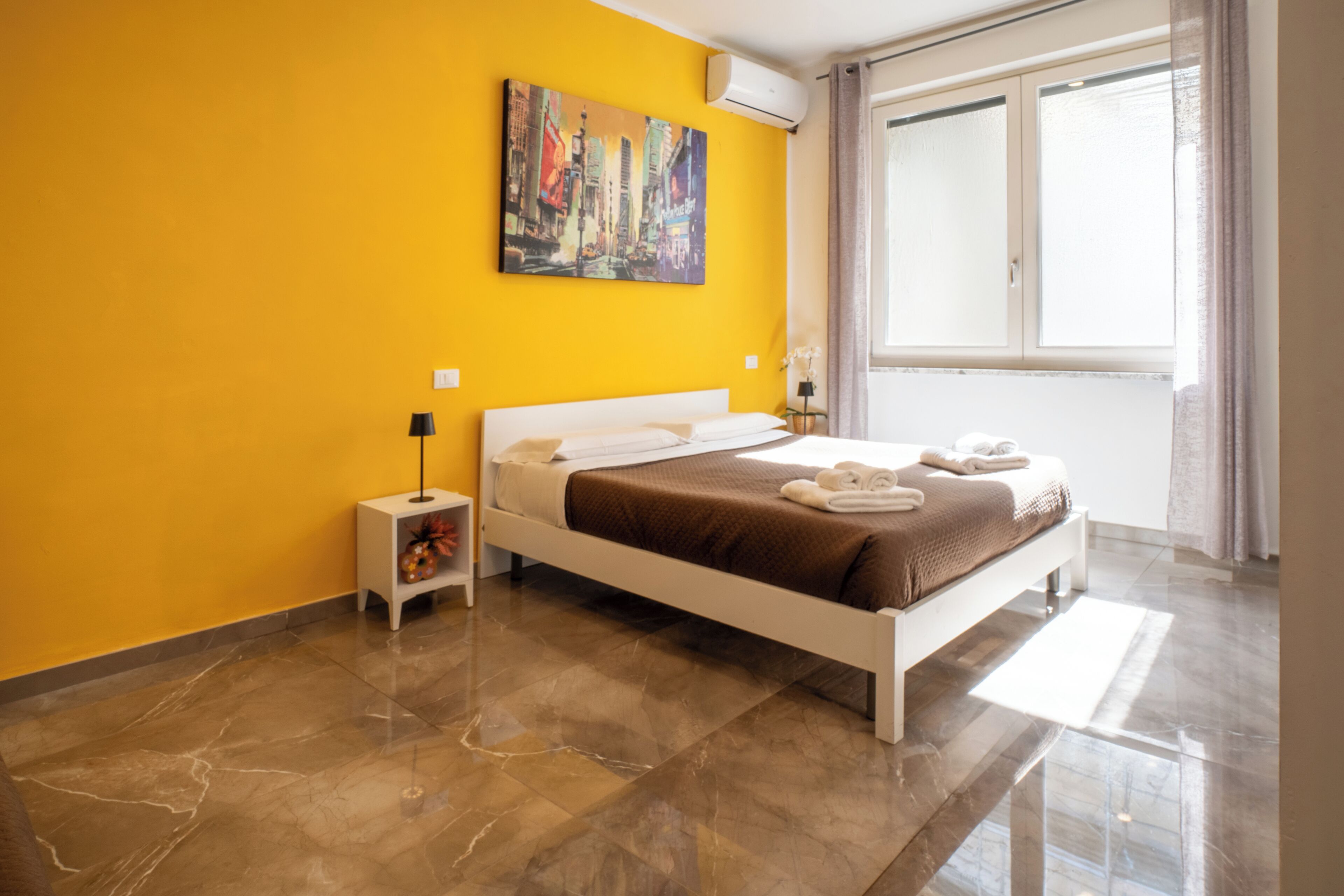 A hotel room with a bed, a nightstand, a painting, and a window.