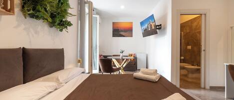 Habitación de hotel con cama, escritorio, silla, baño y vista al atardecer.
