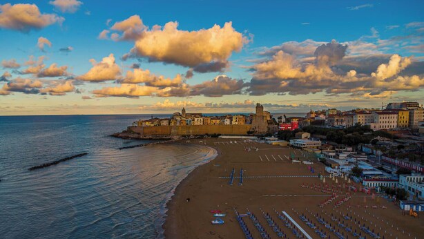 A coastal cityscape with a historic fort, a beach with sun loungers, and a clear sky. - Suebi Central - Deluxe Rooms & Family Suites (Termoli)