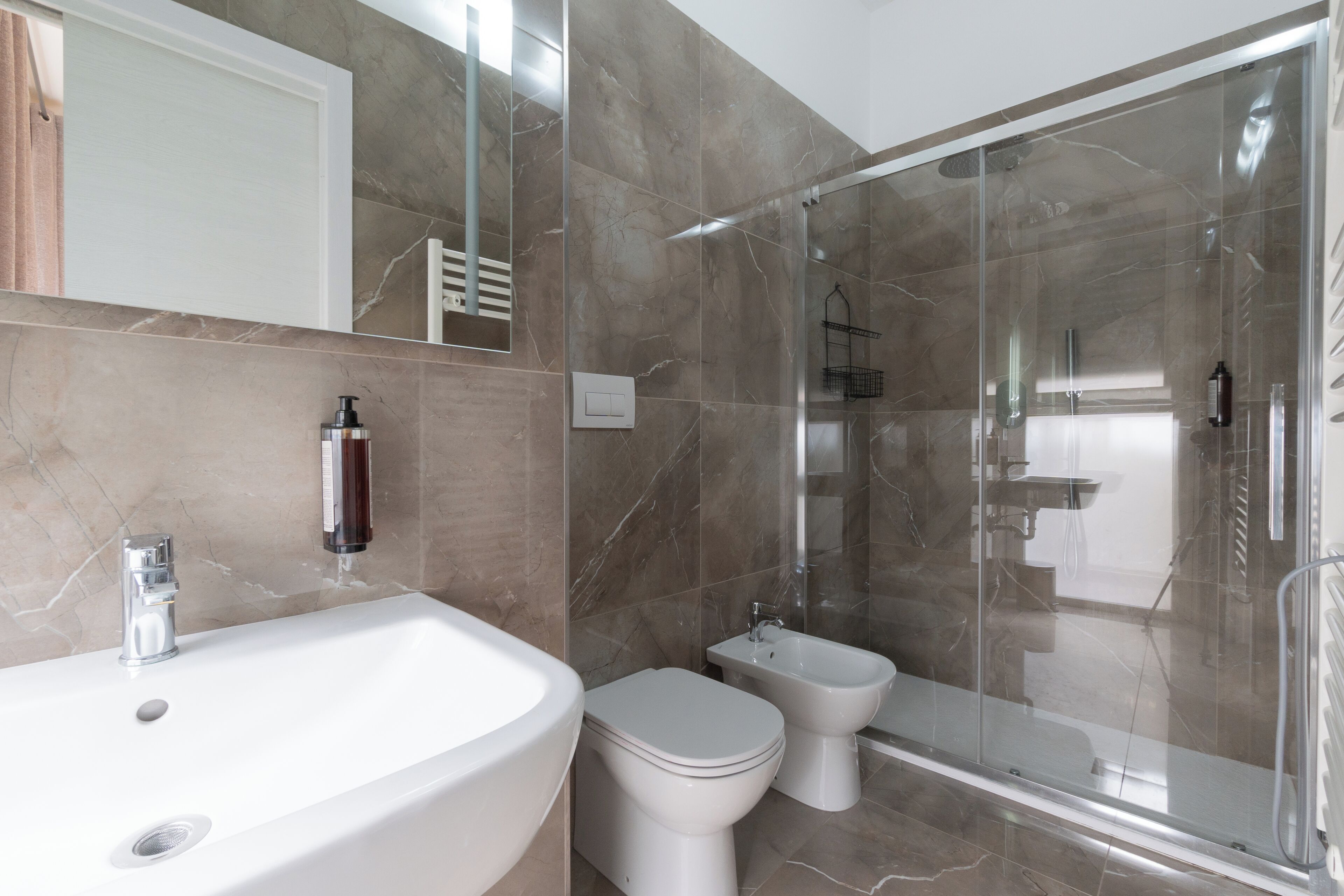 Une salle de bain moderne dotée d’un grand lavabo, de toilettes, d’un bidet et d’une douche séparée par des parois en verre.