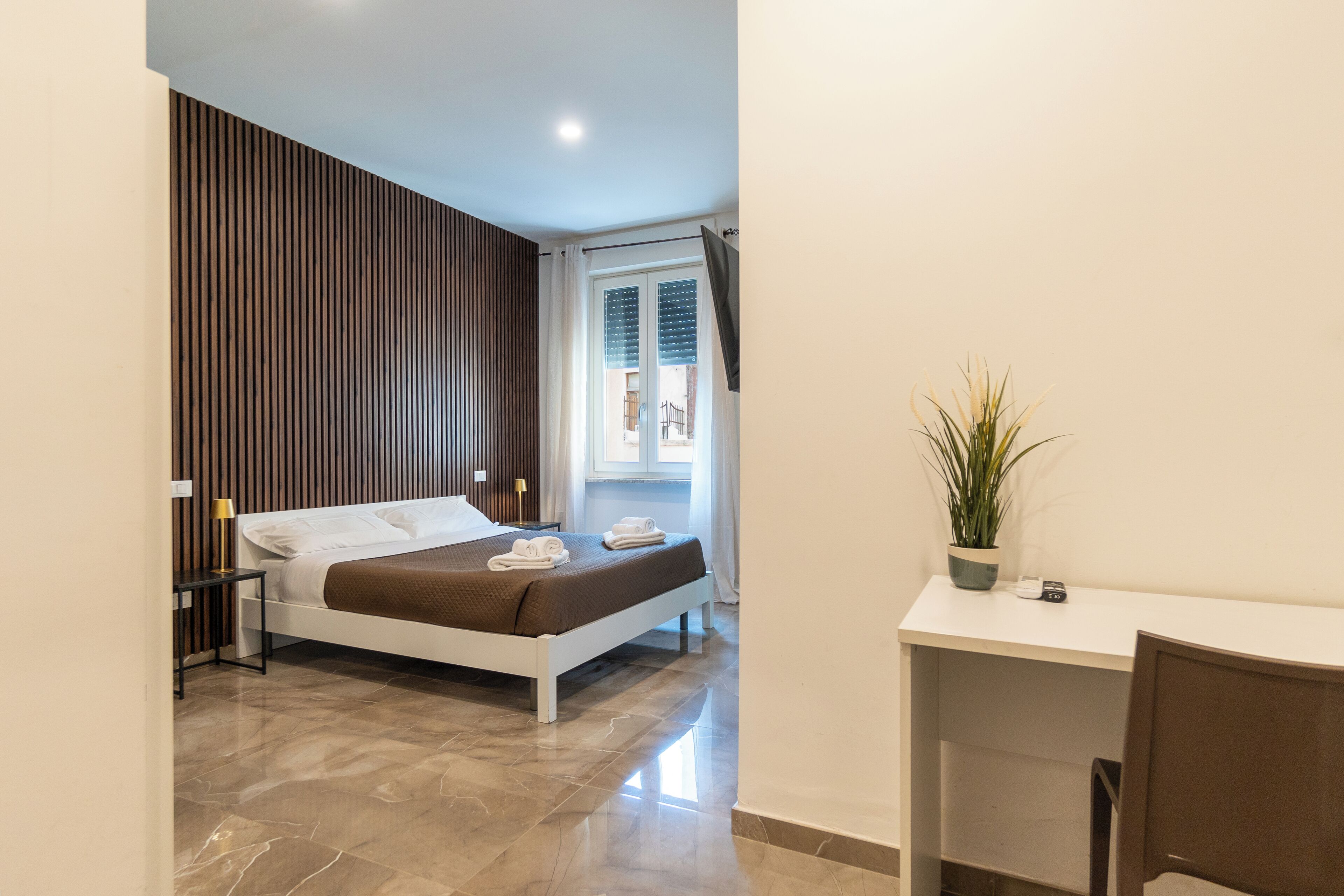 A bedroom with a bed, bedside table, lamp, and a potted plant.