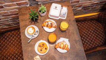 A table with breakfast items including croissants, a coffee drink, and orange juice, set against a brick wall.