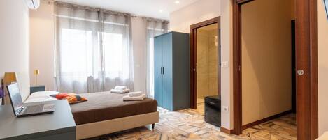 A bedroom with a bed, a desk with a laptop, a wardrobe, and a bathroom with a shower.