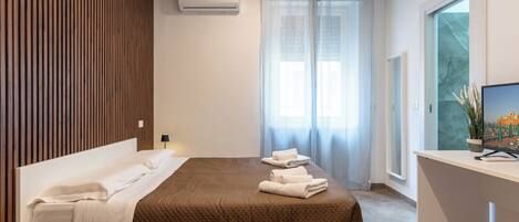A modern hotel room with a bed, a desk, a TV, and a window with curtains.