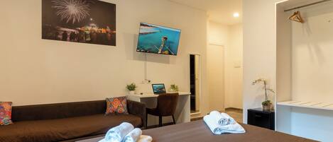 A modern hotel room with a bed, a desk, a TV, and a sofa.