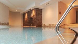 An indoor swimming pool with a stone wall and a metal handrail. - Hotel Nele (Ziano di Fiemme)