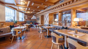 A cozy restaurant with wooden furniture, a fireplace, and large windows. - Hotel Nele (Ziano di Fiemme)