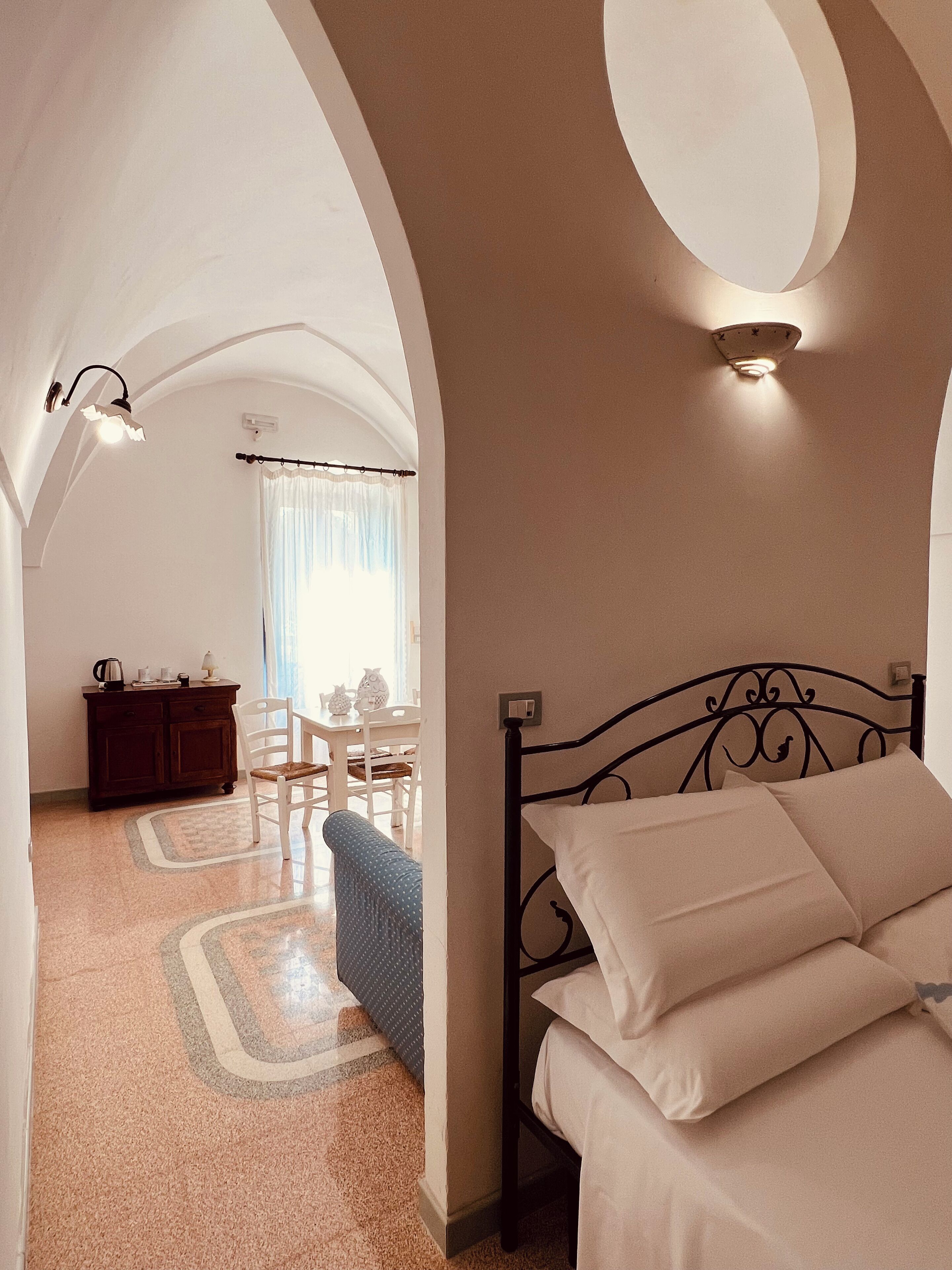 Ein Schlafzimmer mit einem Bett, einem Schreibtisch und einem Stuhl. Es gibt ein Fenster mit Vorhängen, eine Deckenleuchte und eine Wandlampe.