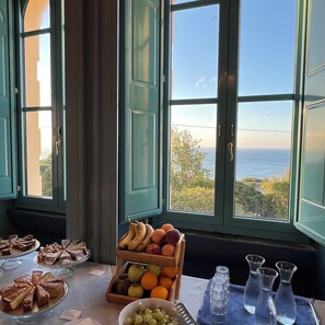 A table with a fruit display and desserts, a view of the sea through large windows.