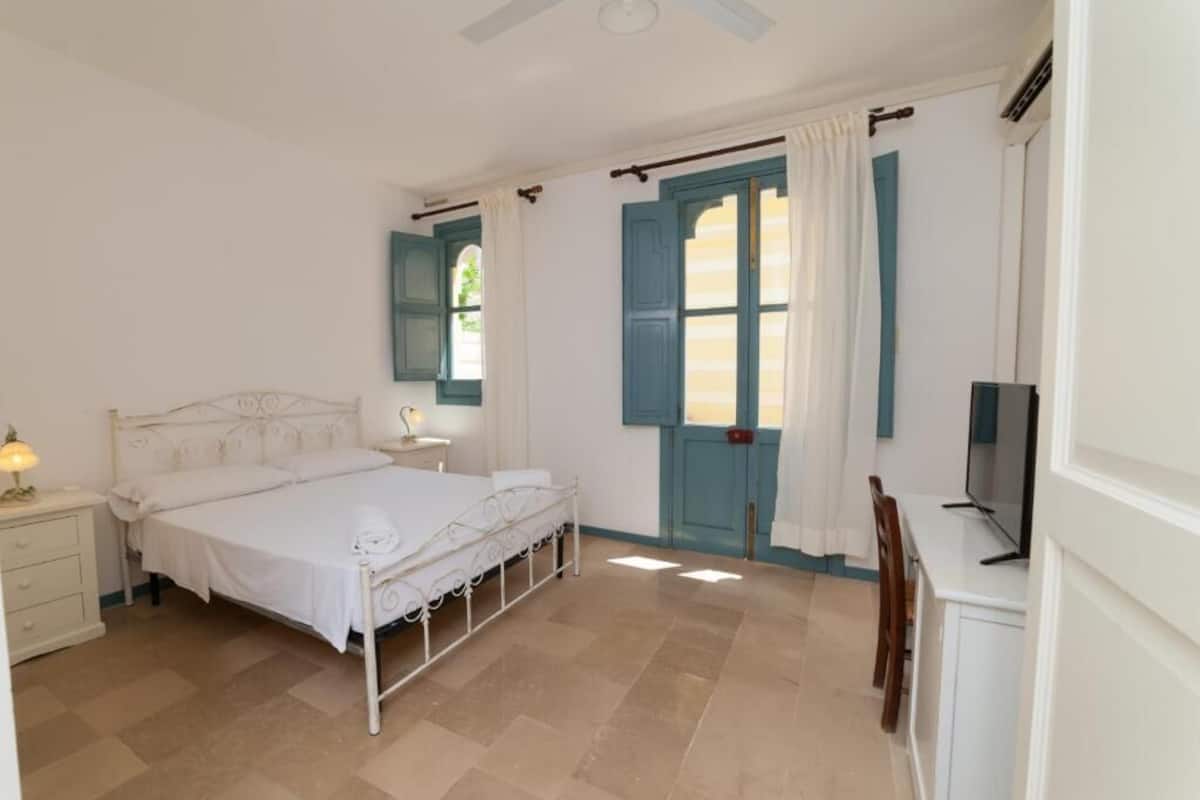 A bedroom with a bed, bedside table, lamp, and a television.
