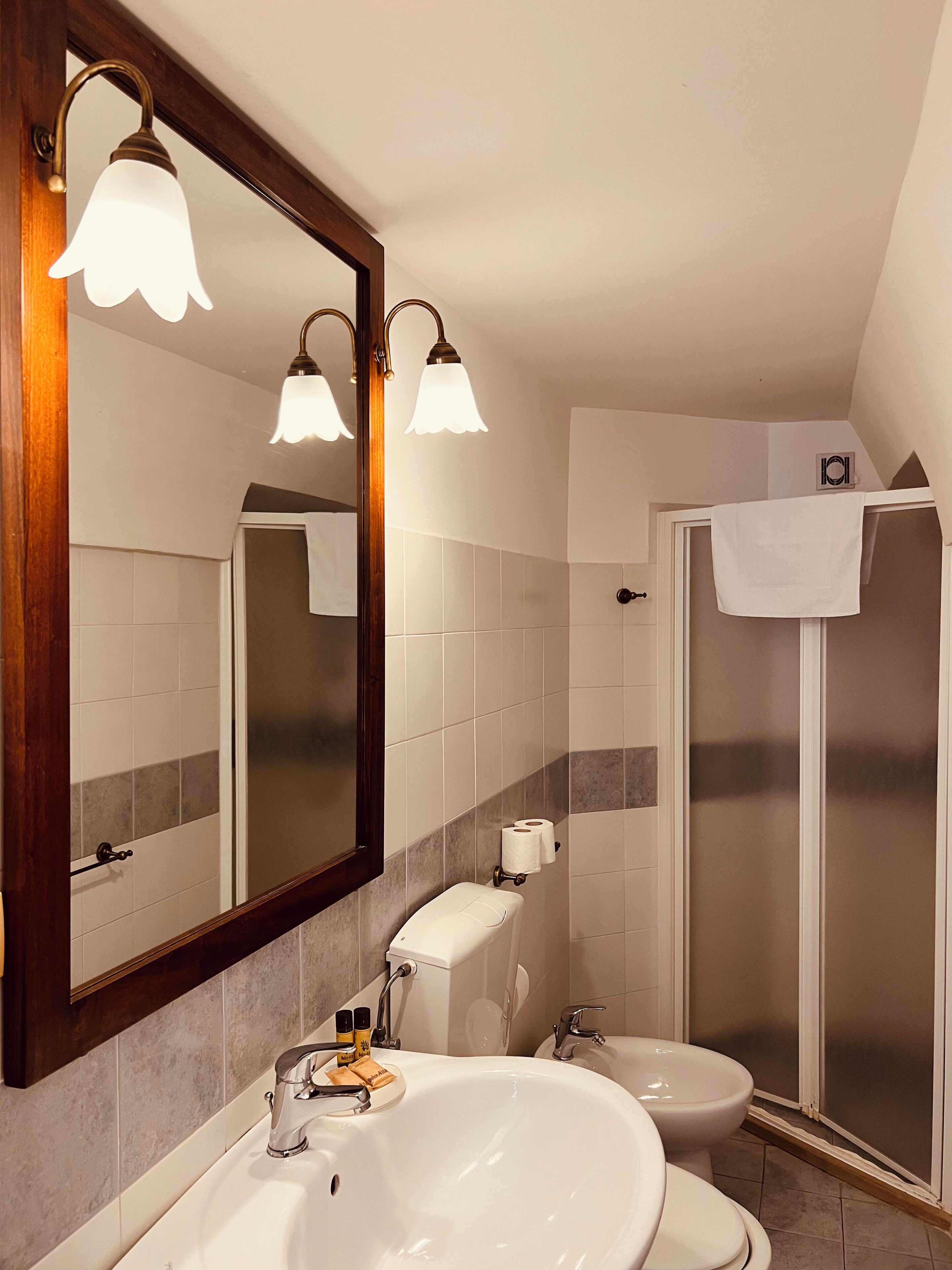 Une salle de bain dotée d’un grand miroir, de deux lavabos, de toilettes et d’une douche à parois de verre.