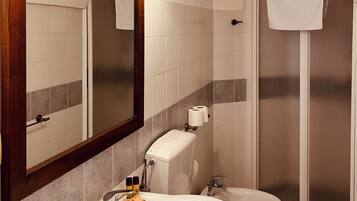 Une salle de bain dotée d’un grand miroir, de deux lavabos, de toilettes et d’une douche à parois de verre.
