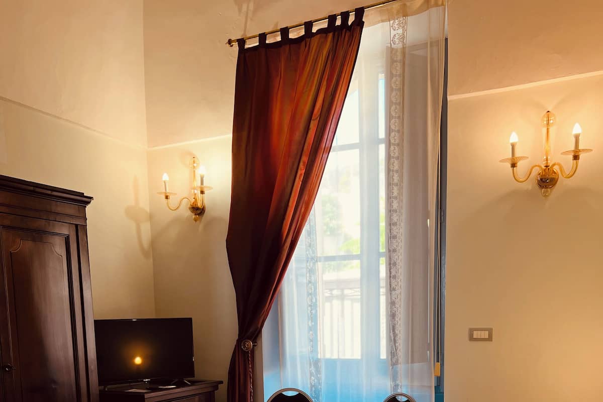 A hotel room with a bed, a TV, a wardrobe, two chairs, and a view of a balcony.