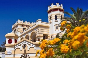 Hotel features a distinctive tower with battlements and a balcony, surrounded by a garden with arches and windows.