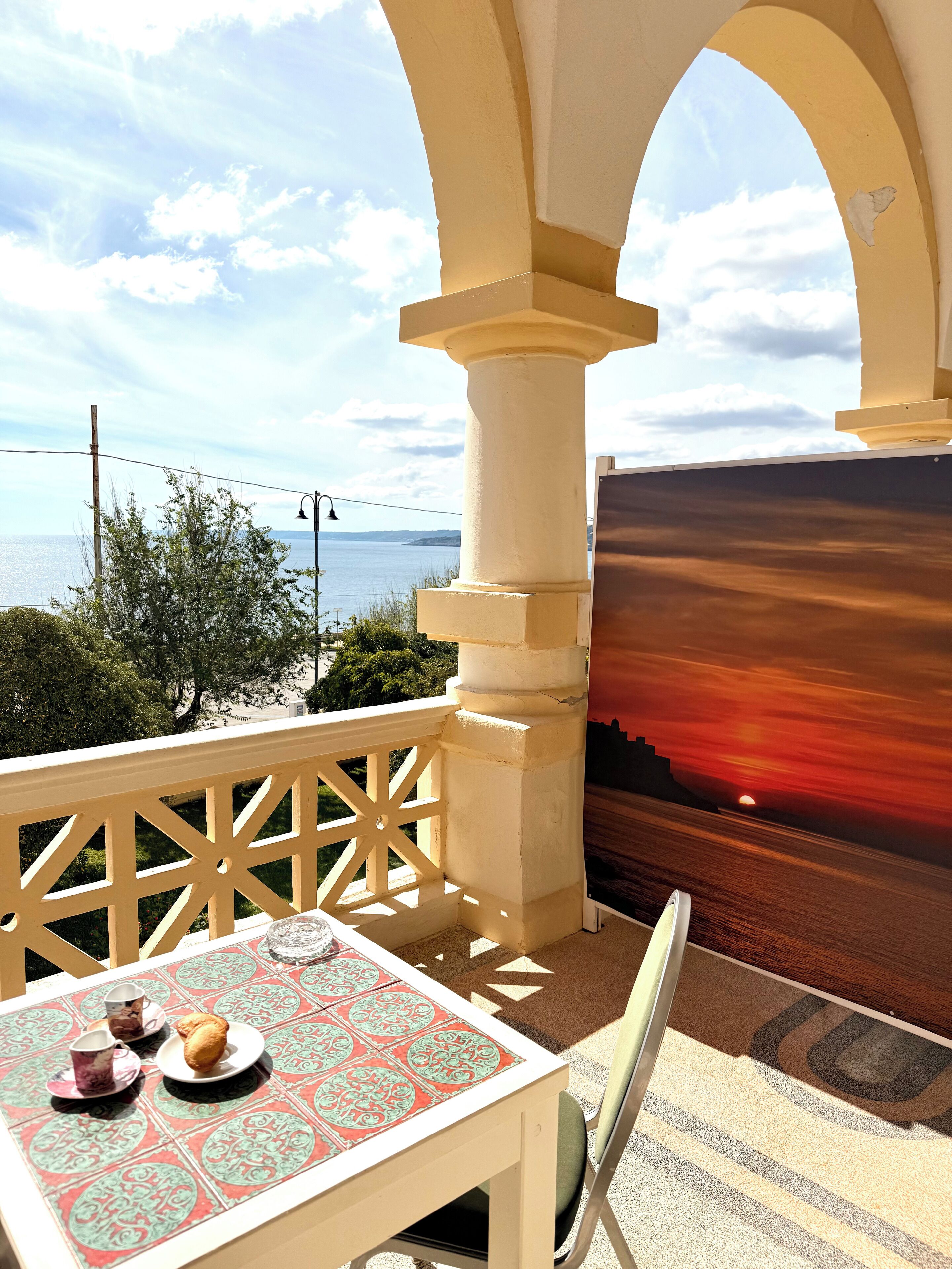 Varanda com mesa posta para dois, oferecendo vista panorâmica do mar e do pôr do sol.