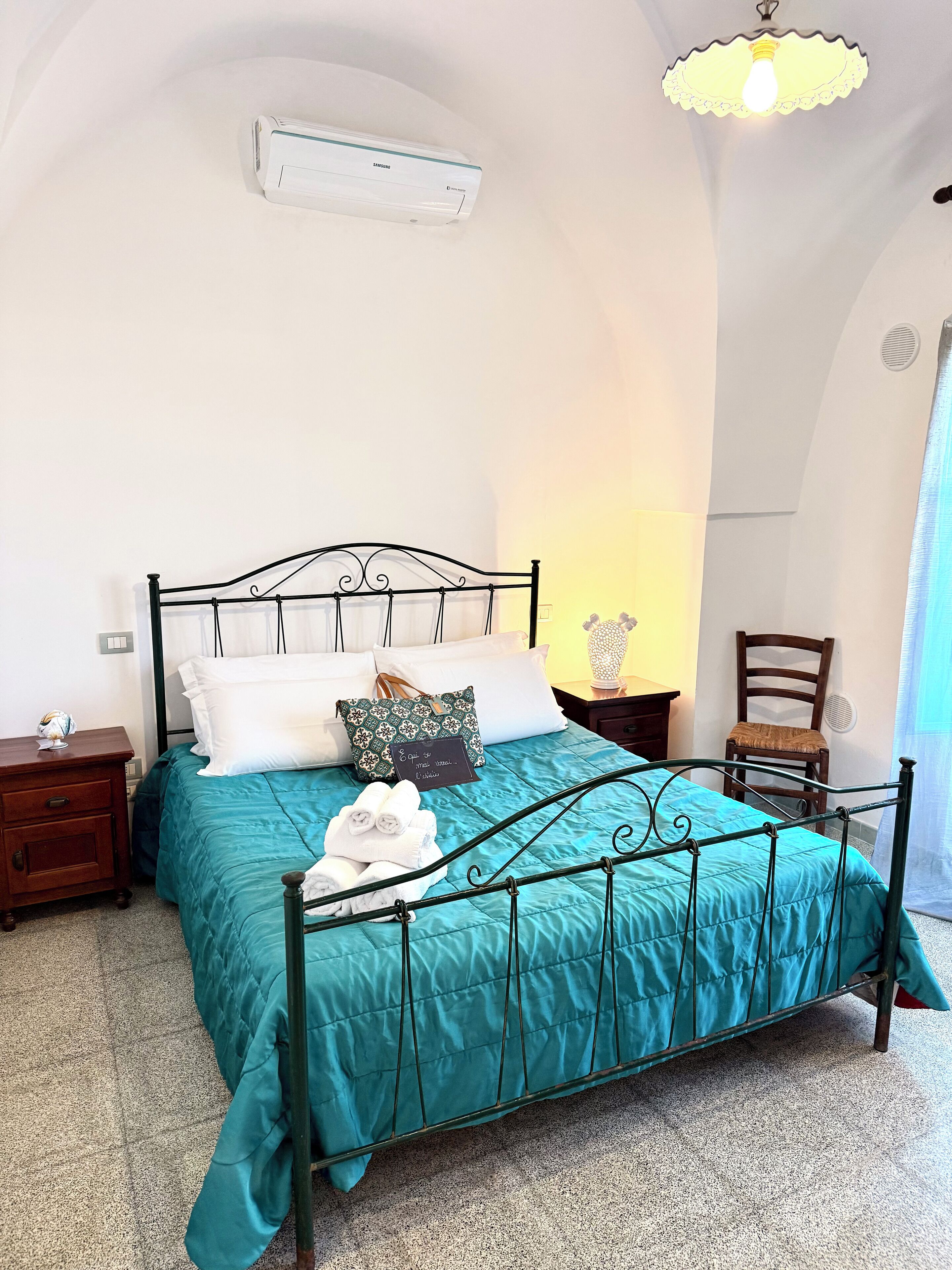 A neatly made bed with a teal bedspread, a black metal headboard, and a bedside table with a lamp.