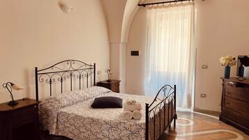 Un dormitorio con cama, mesita de noche, cómoda y ventana con cortinas.