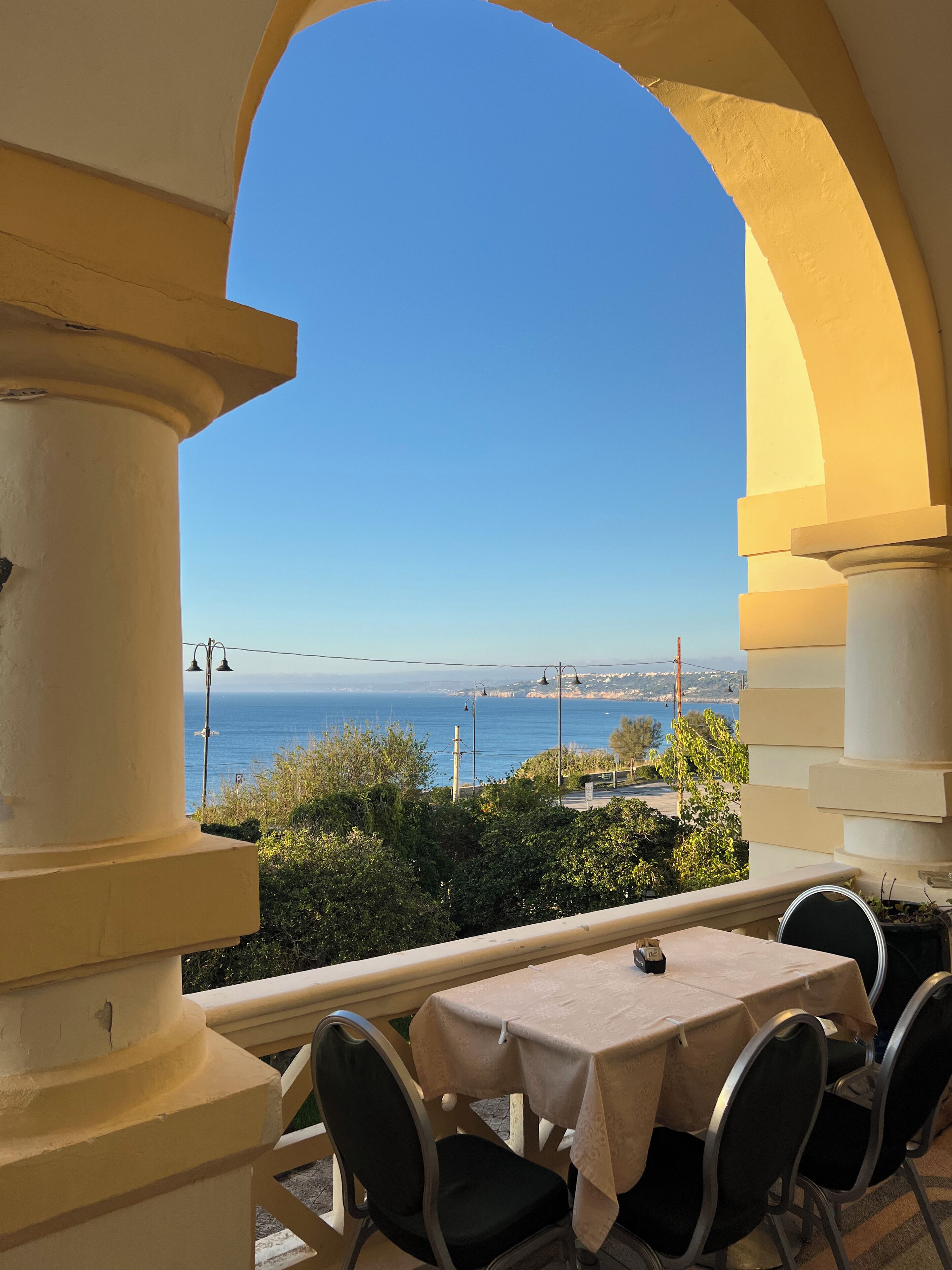 Un balcón con mesa y sillas, con vistas a la costa, el mar y tierra distante.