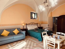 Una habitación con sofá, cama, mesa con sillas y techo de diseño abovedado.