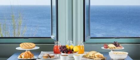 Una mesa de desayuno con cruasanes, fruta y jugo, con vista al mar.