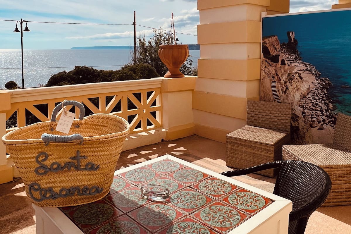 A terrace with a table, wicker chairs, a wicker basket, and a view of the sea.