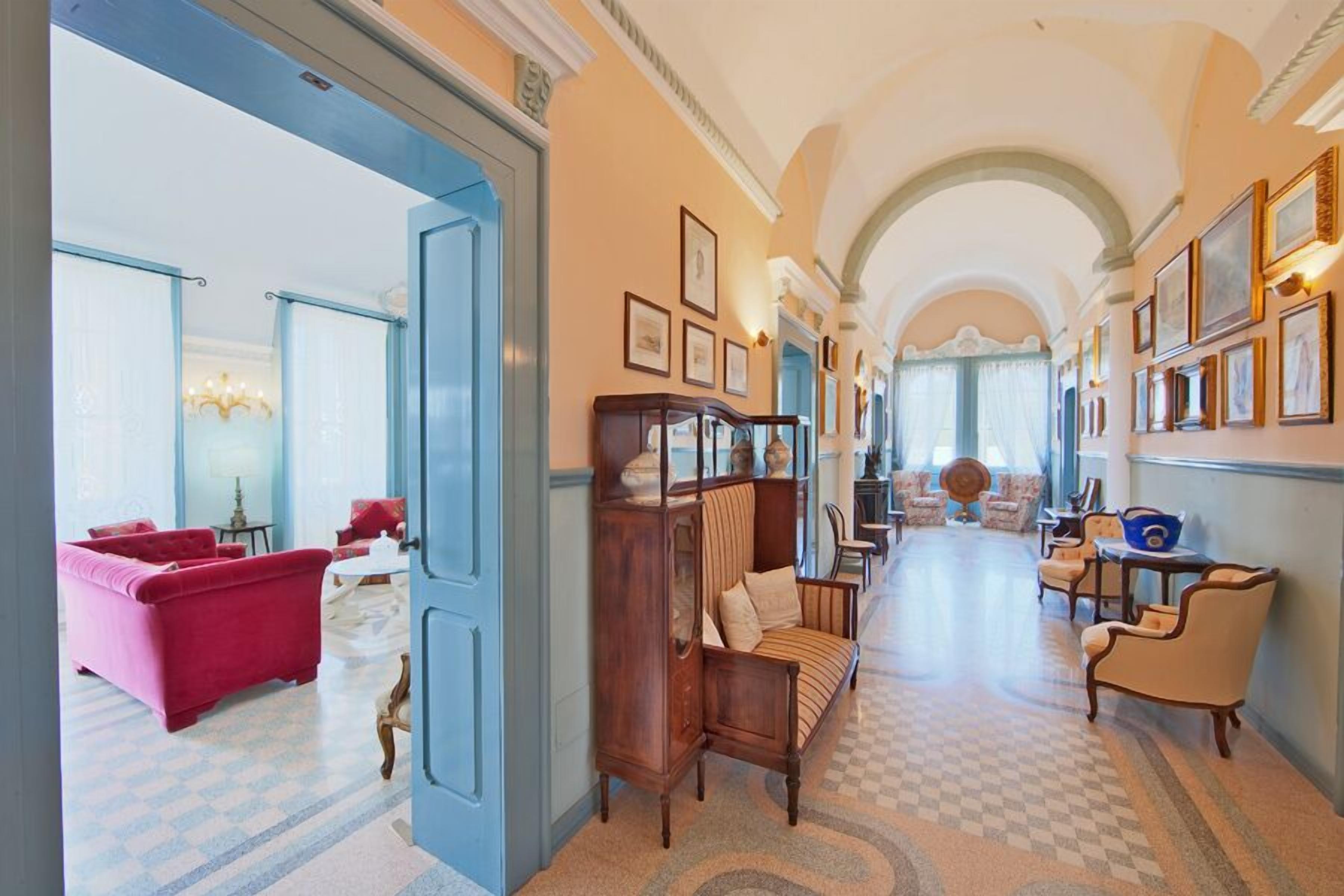 A hallway with a checkered floor, a red armchair, a wooden cabinet, and a blue door.