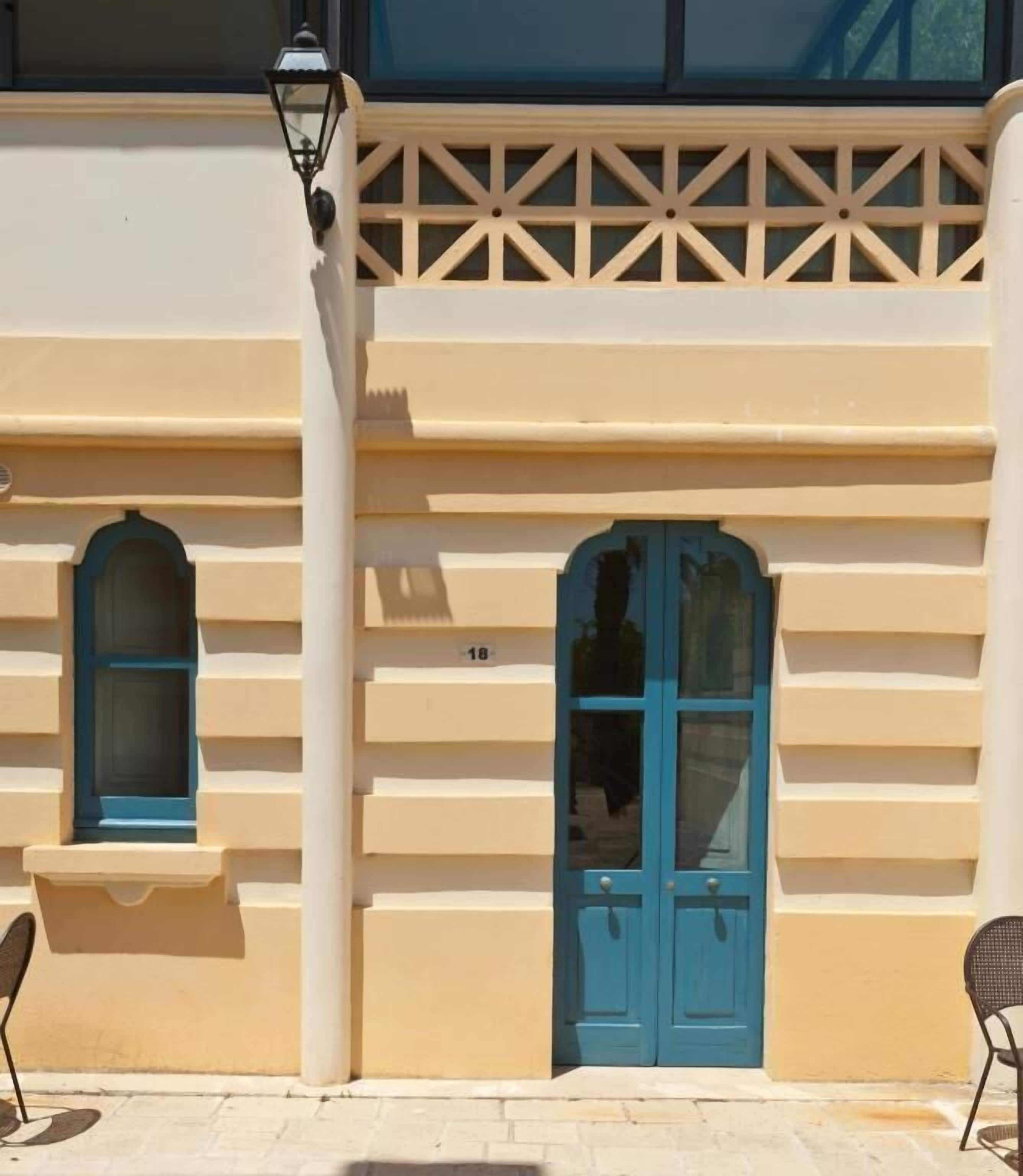 Un edificio con fachada color crema, dos puertas azules y una ventana pequeña con marco azul.