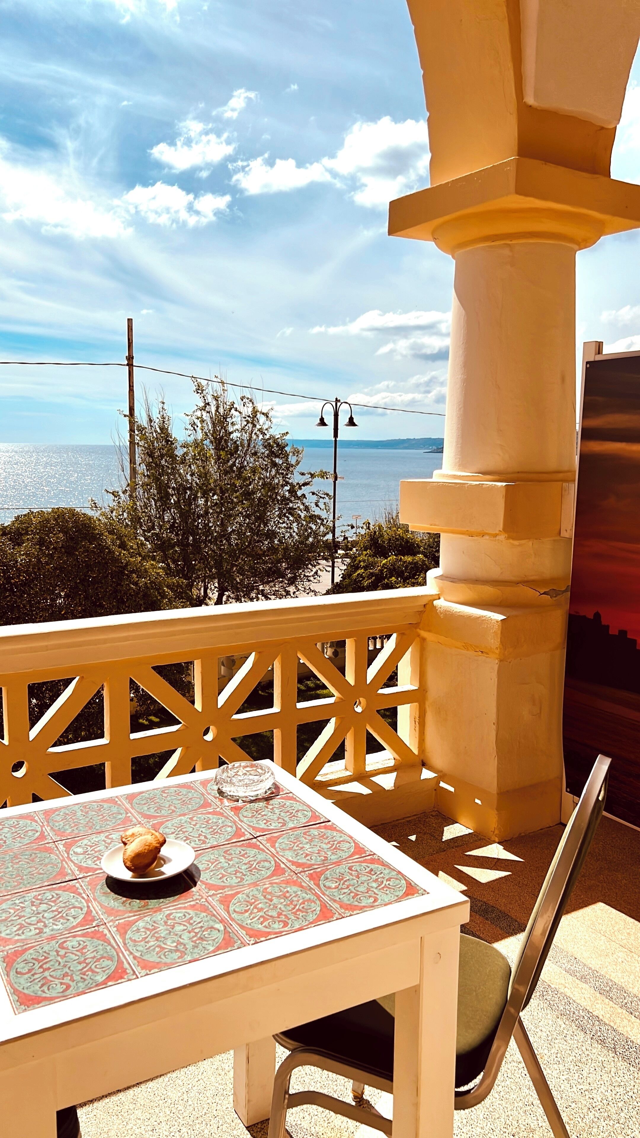 A balcony with a table, a chair, and a view of the sea.