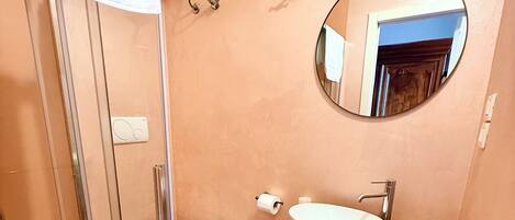 A bathroom with a glass shower enclosure, a white toilet, a wooden vanity with a white sink, and a round mirror.