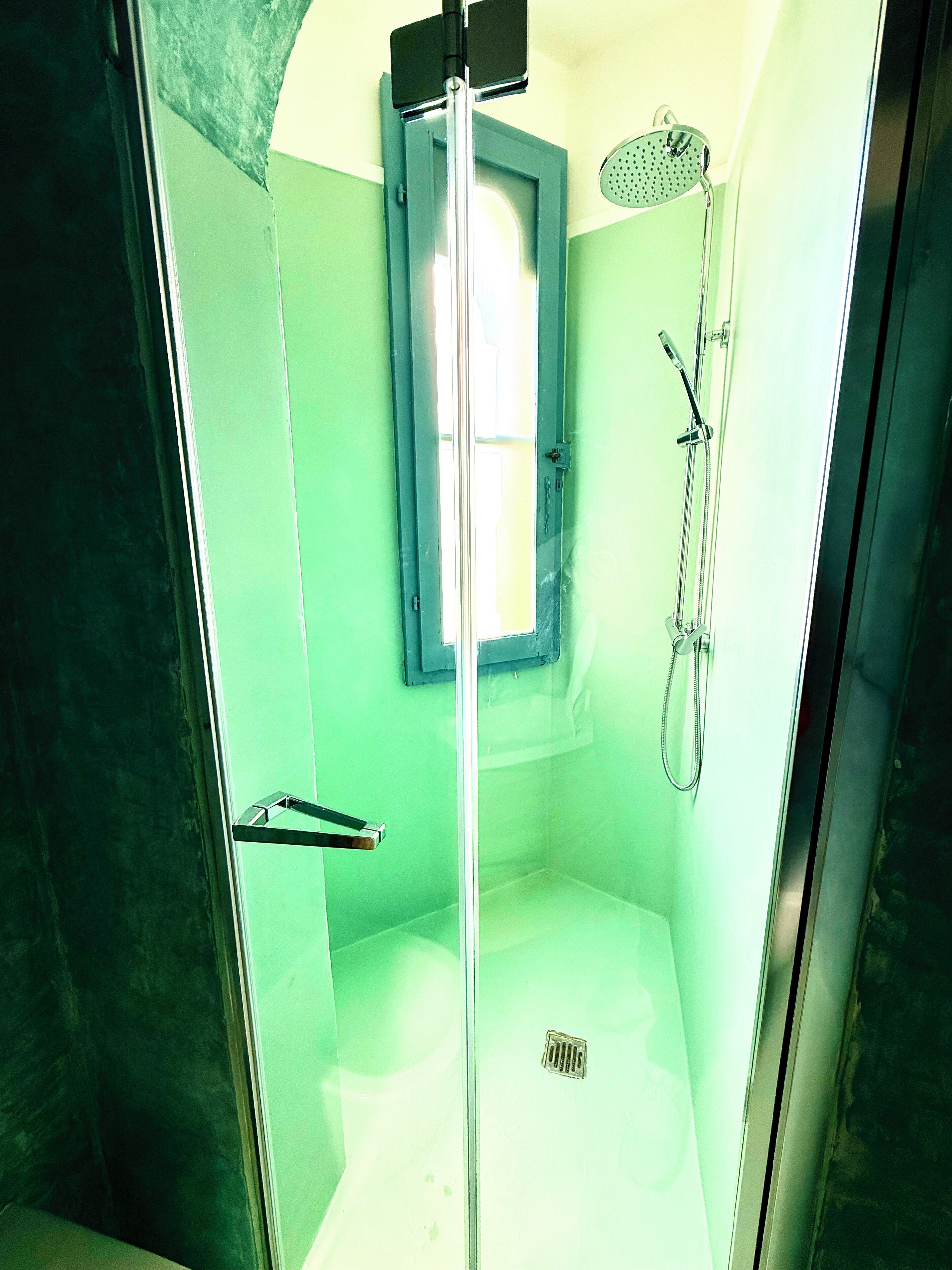 A glass-enclosed shower stall with a handheld showerhead and a handheld shower attachment.
