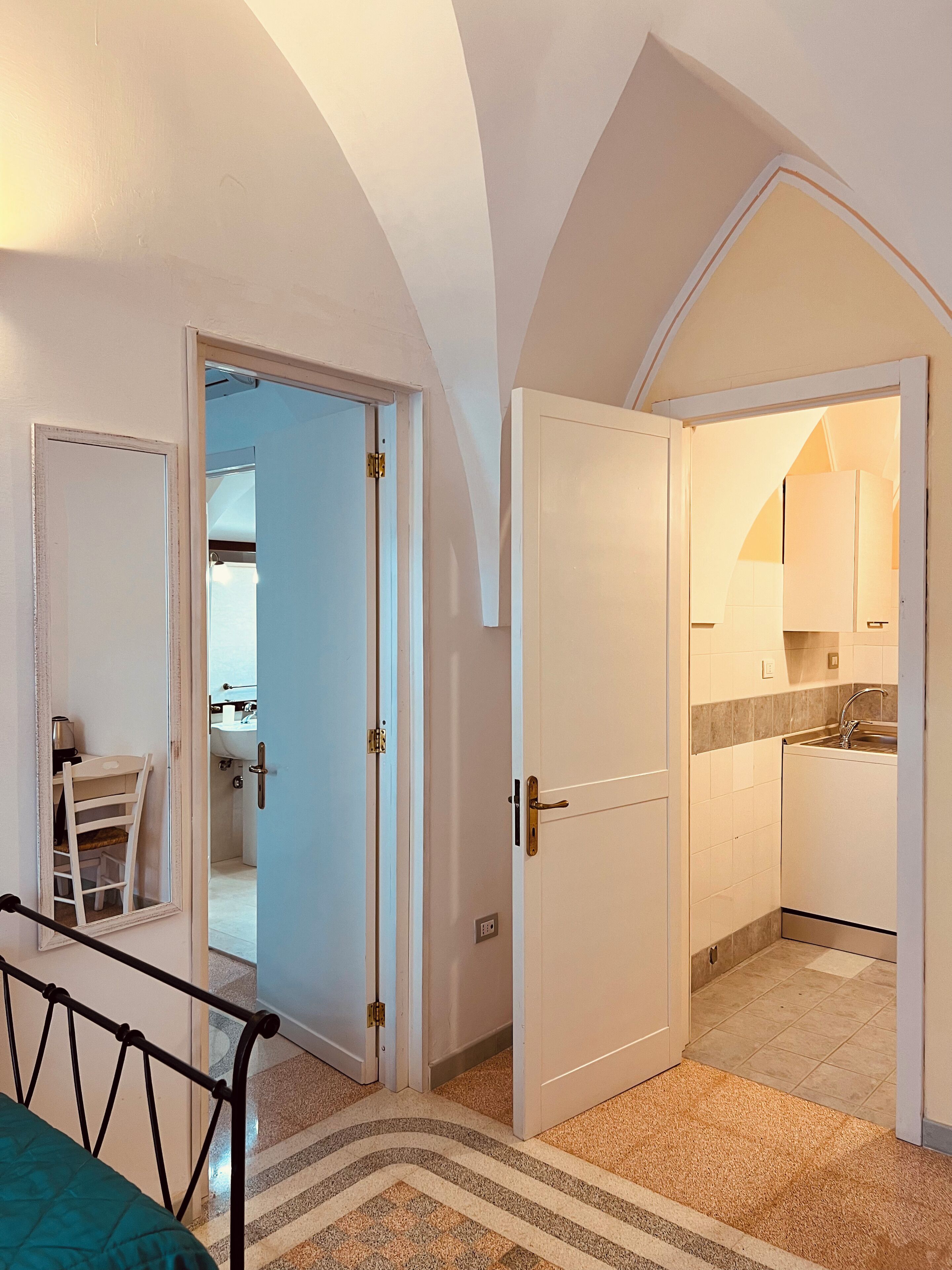 A room with a bed, a chair, and an open door leading to a kitchen with a sink and cabinets.
