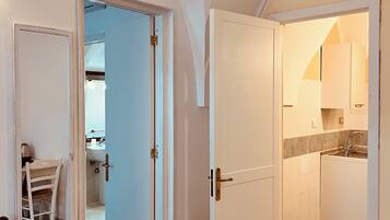 A room with a bed, a chair, and an open door leading to a kitchen with a sink and cabinets.