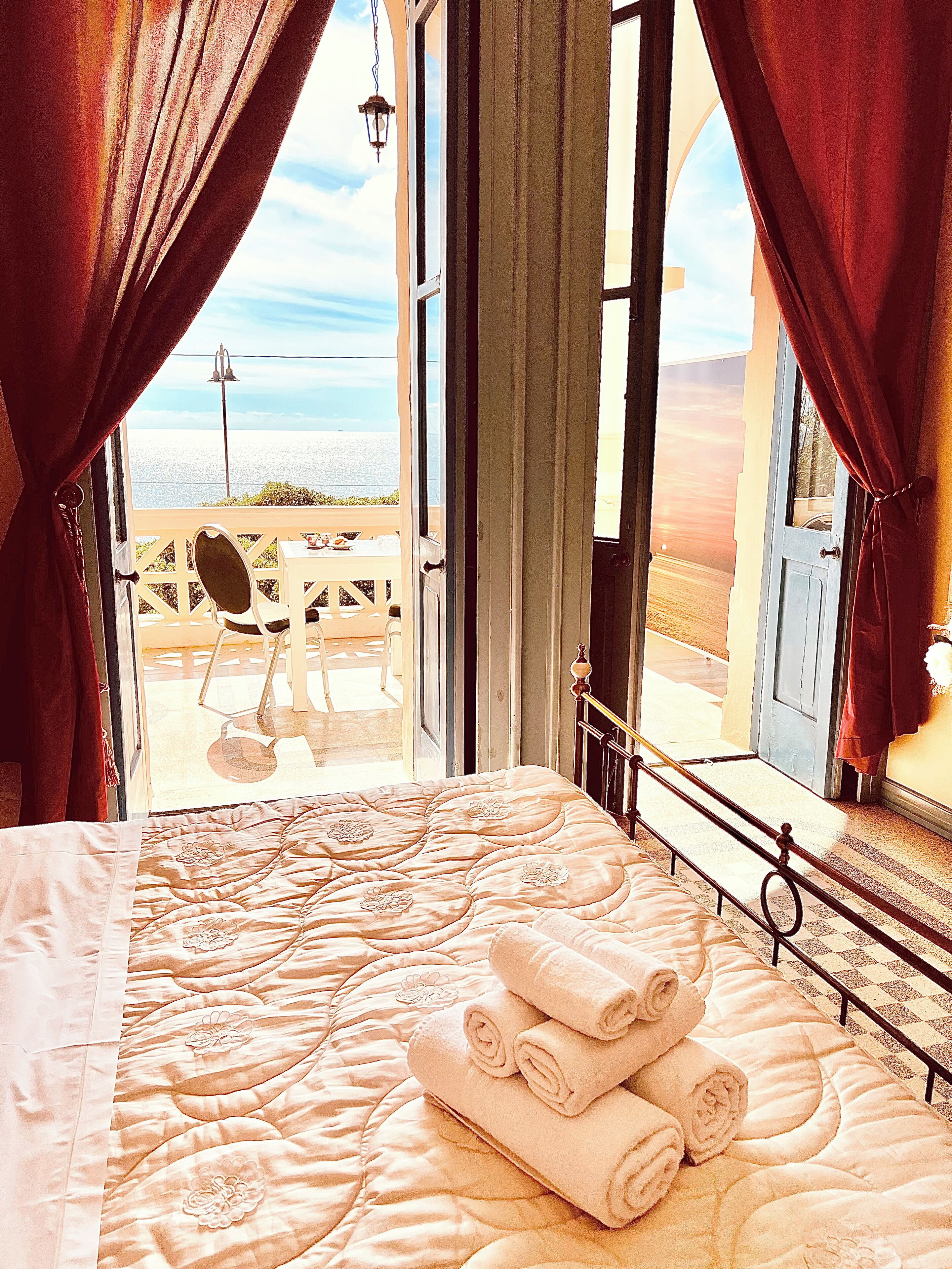 Un lit avec des serviettes pliées, une vue sur la mer et un balcon avec une table et des chaises.