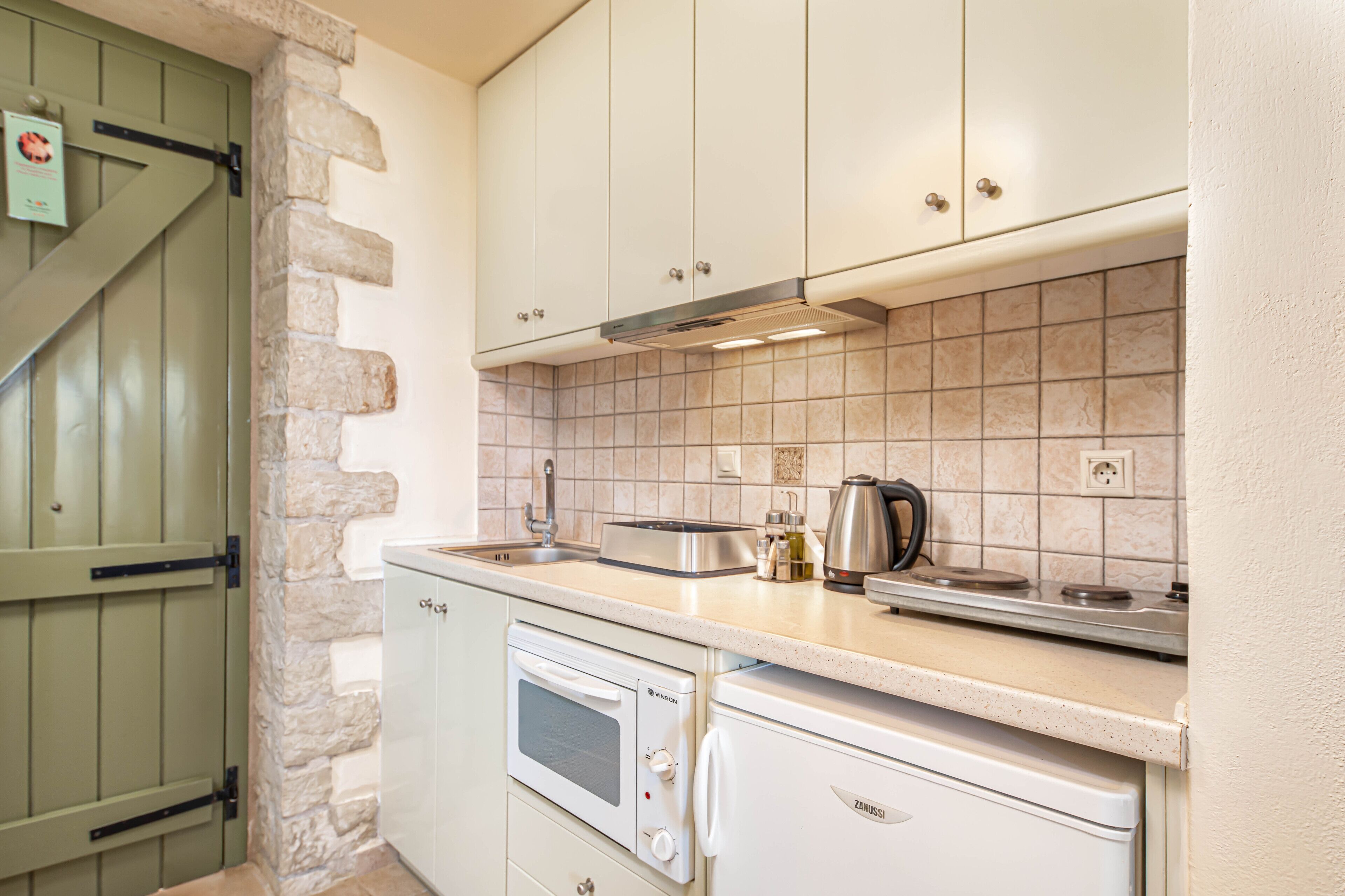 A kitchen with white cabinets, a stone wall, a green door, and a tiled backsplash.