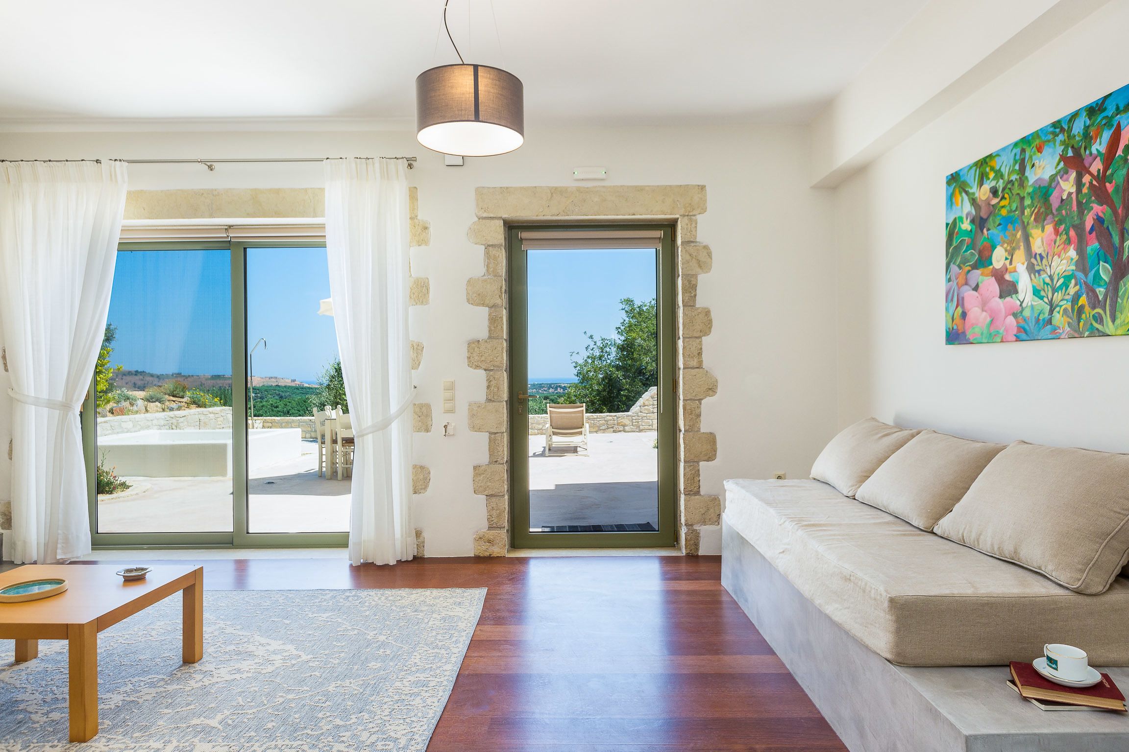 Una sala de estar con sofá, una mesa y vista a un patio exterior a través de un ventanal.