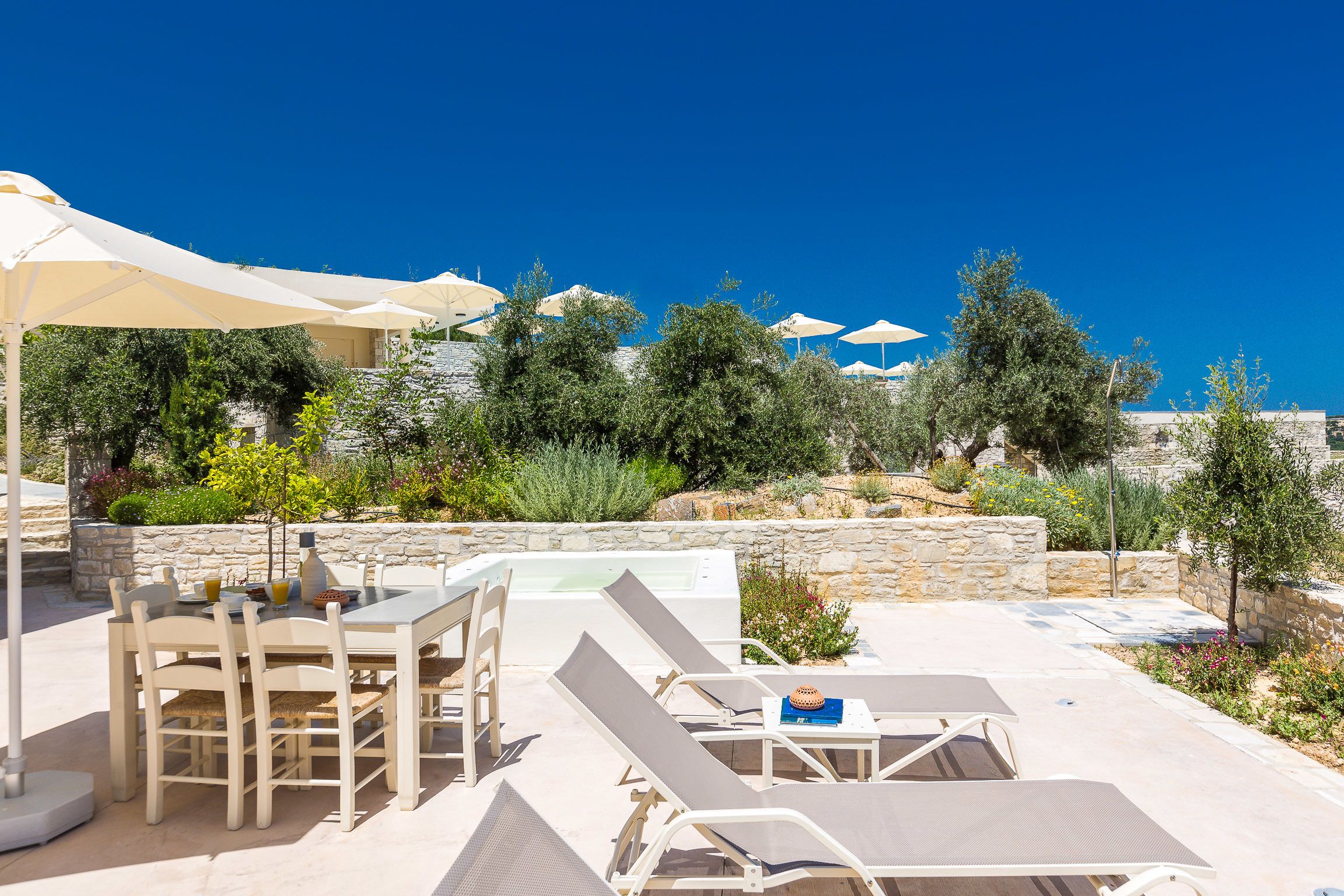 Een zonnig terras met een tafel, stoelen, loungezetels en parasols.