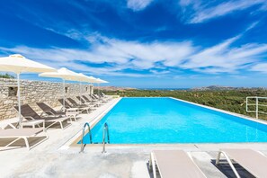 Una piscina con sillas de descanso y sombrillas, rodeada de muros de piedra y vistas al paisaje.