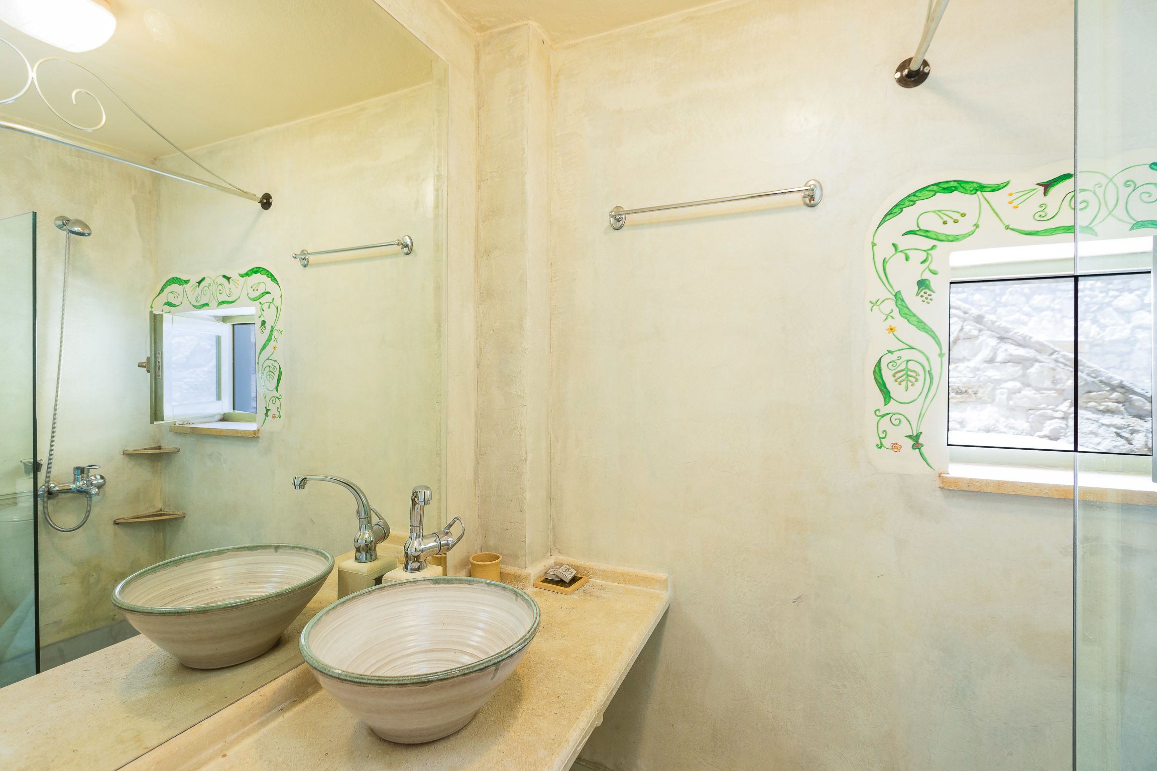A bathroom with a large glass shower enclosure, a double sink with a bowl design, and a mirror with a decorative frame.