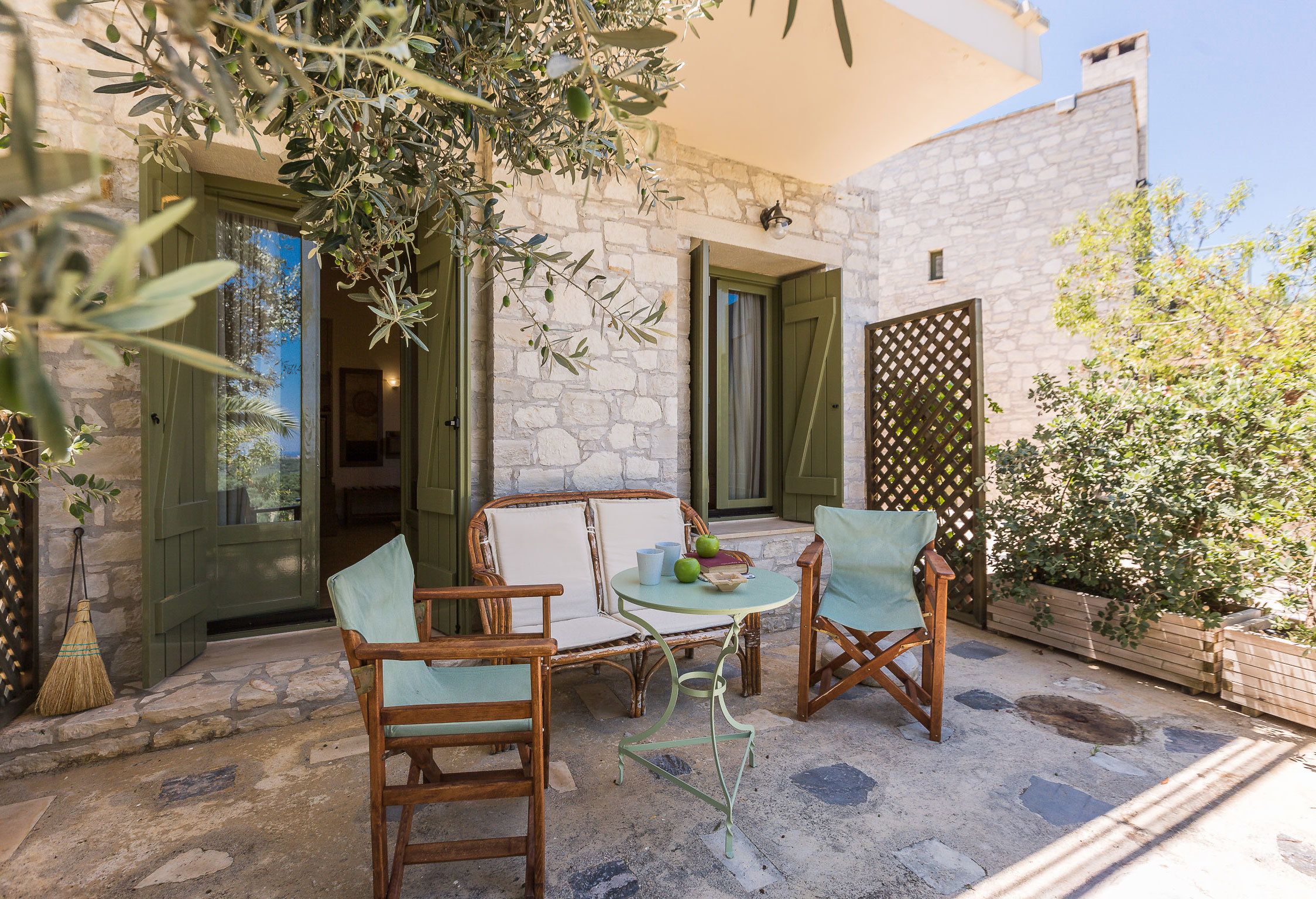 An outdoor seating area with wicker chairs and a table, stone walls, and a wooden fence.