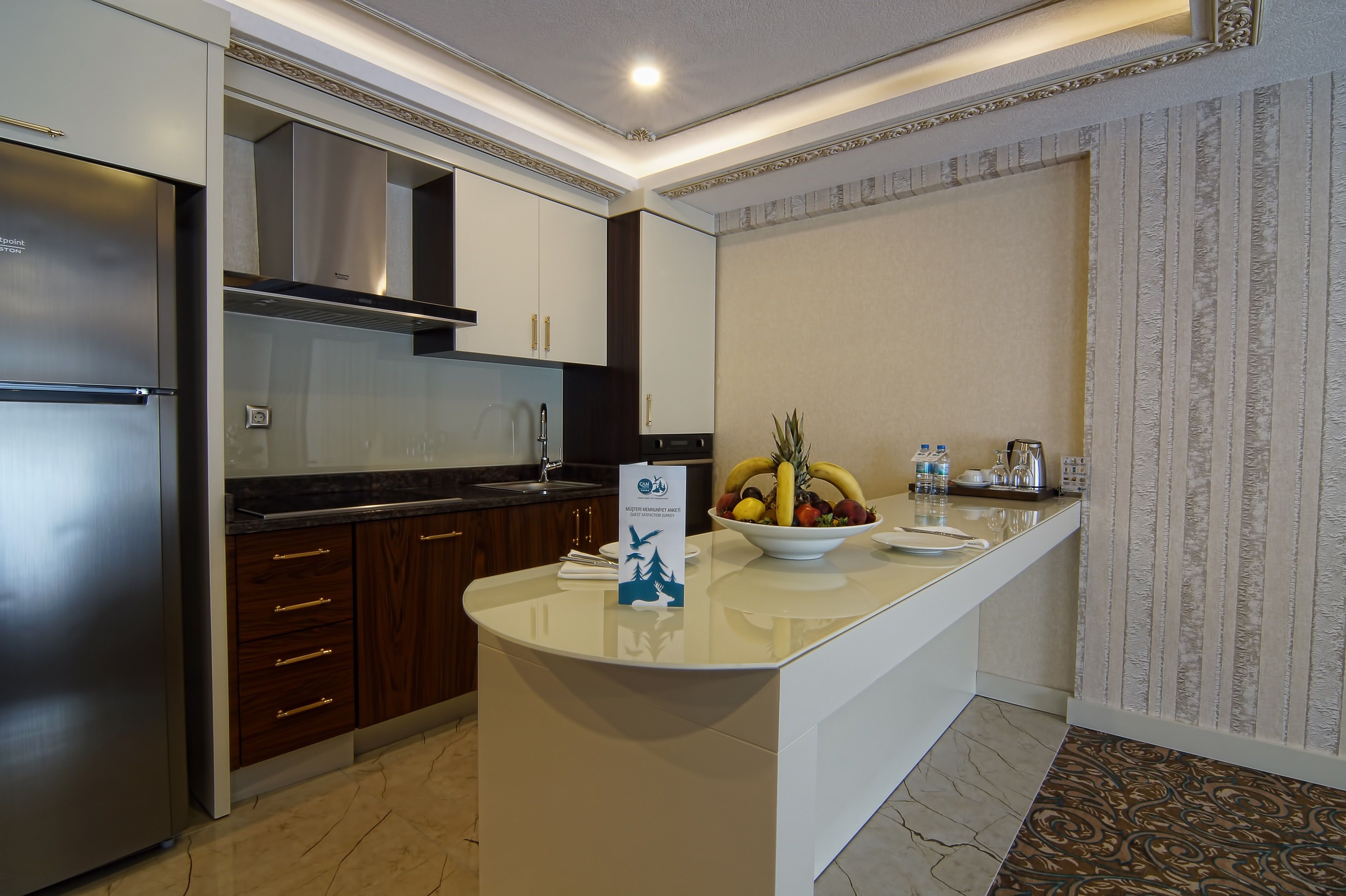 A modern kitchen with a stainless steel refrigerator, wooden cabinets, and a central island with a fruit bowl.