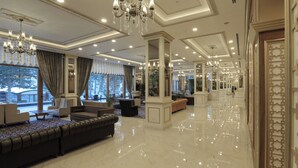 A spacious lobby with a large sofa, elegant chandeliers, and a polished marble floor.