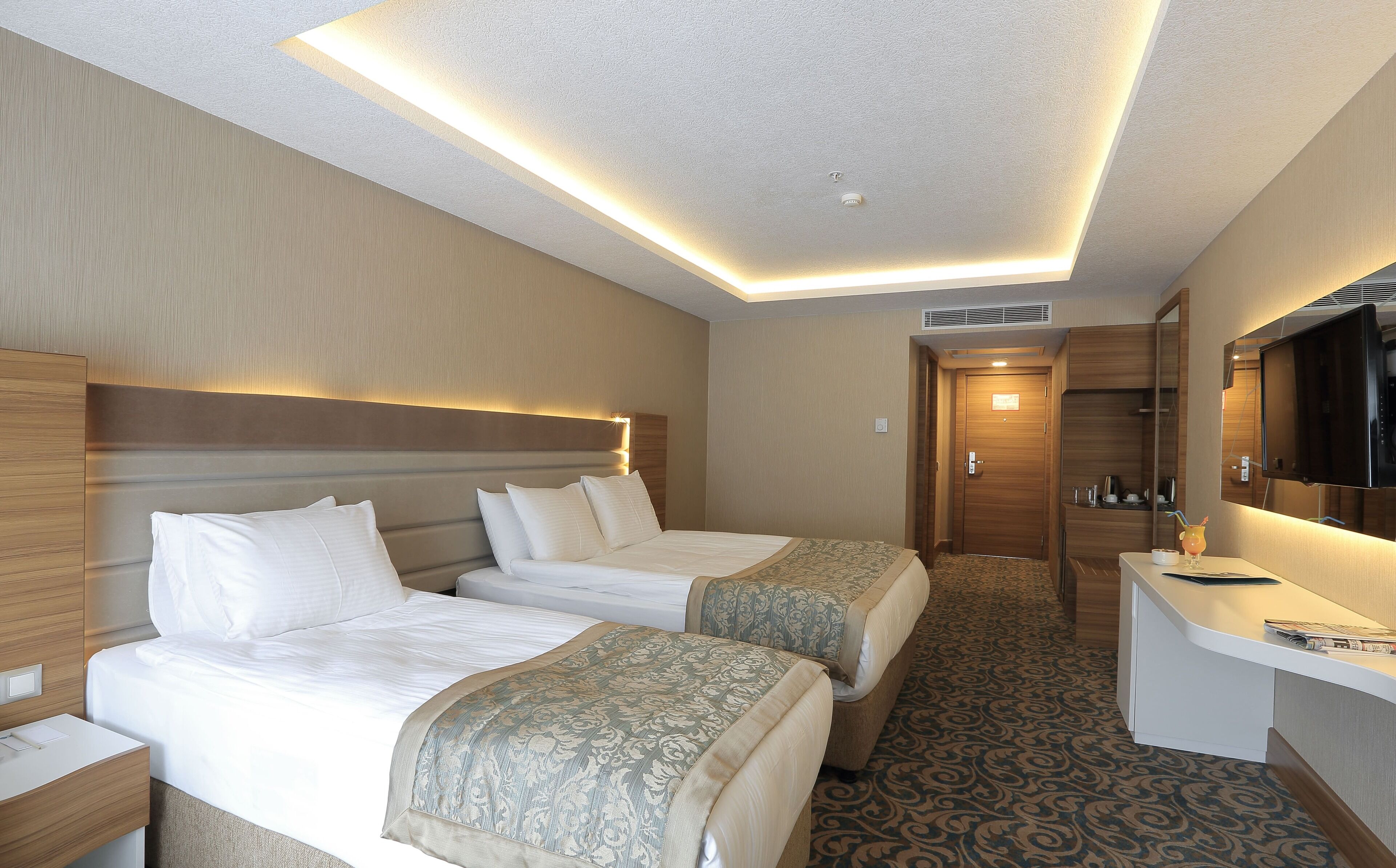 A hotel room with two beds, a desk, a mirror, and a television.
