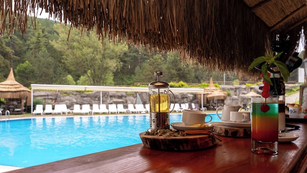 A bar area with a view of a swimming pool, a coffee machine, and a glass of drink.