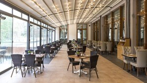 A spacious indoor dining area with long tables and chairs, large windows, and a modern ceiling design.