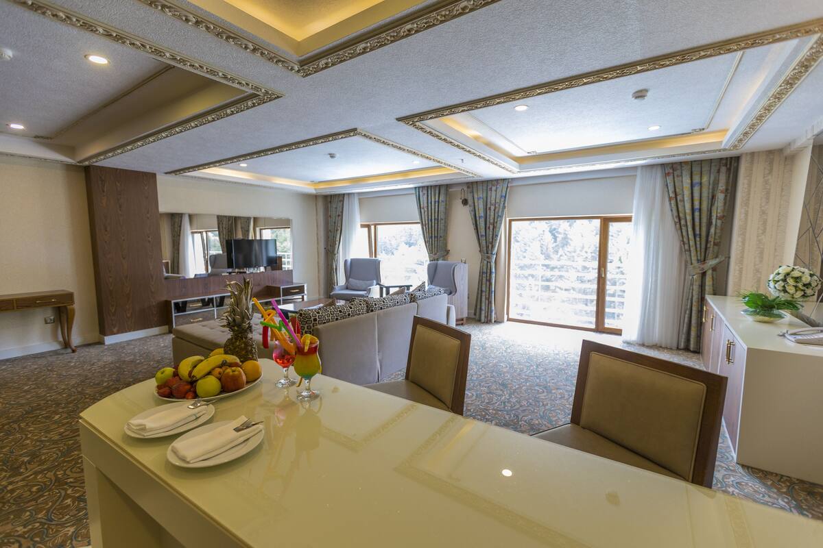 Een restaurantgedeelte in een hotel, met een grote tafel, stoelen, een schaal fruit en een televisie.