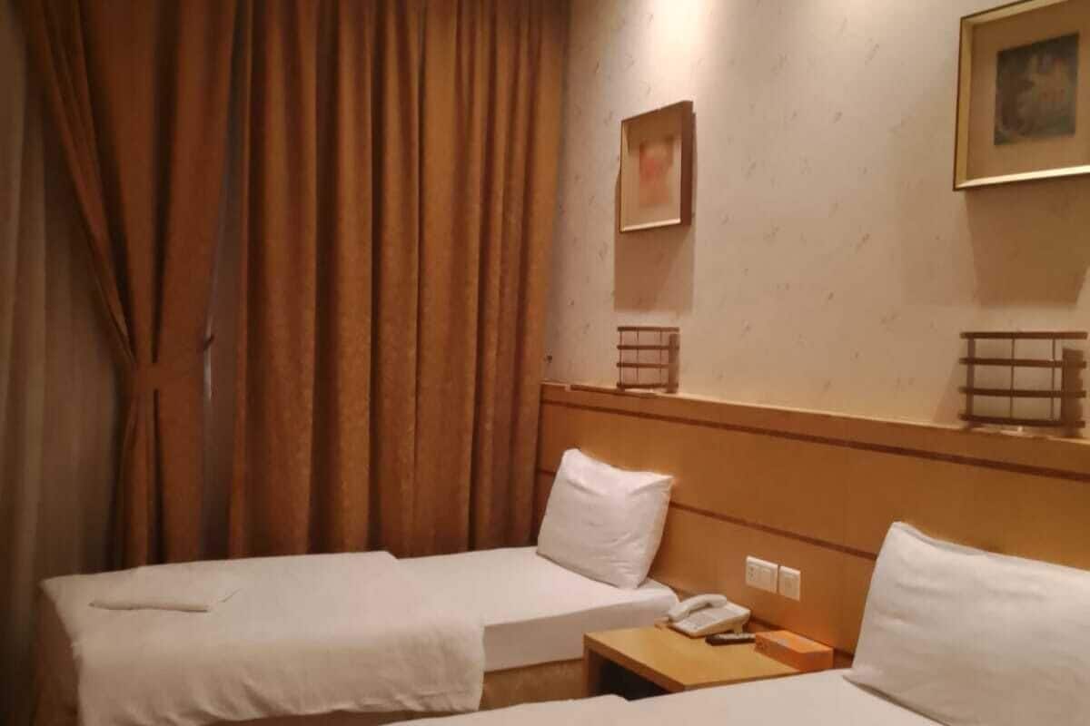 Une chambre d’hôtel avec deux lits, une tête de lit en bois, une table de chevet avec un téléphone et un tableau au mur.