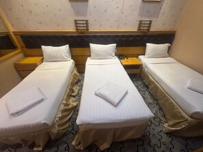 Ein Hotelzimmer mit drei Einzelbetten, jeweils mit weißer Bettdecke und ordentlich gefalteten Handtüchern.