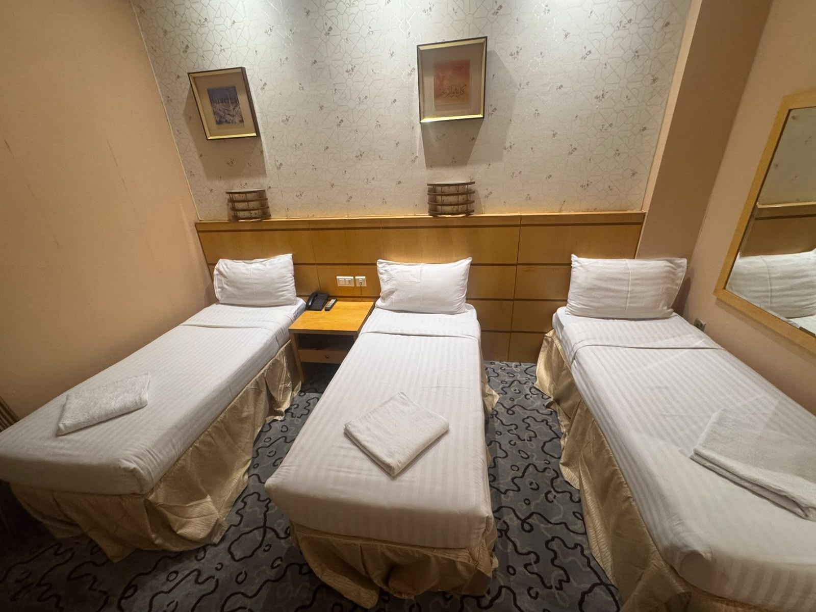 Habitación de hotel con dos camas individuales, una mesita de noche de madera, un teléfono y una lámpara de pared.